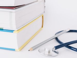 stacked-books-pencil-stethoscope-white-surface