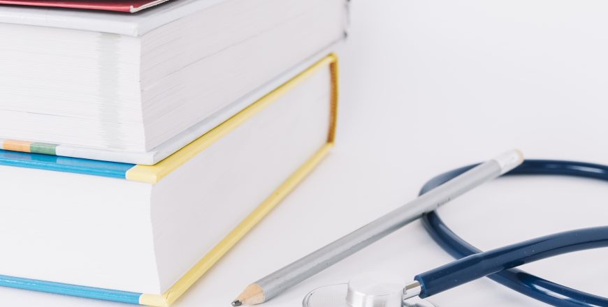 stacked-books-pencil-stethoscope-white-surface