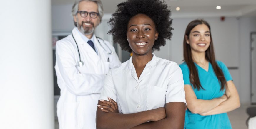 multiethnic-group-three-doctors-nurses-standing-hospital-corridor-wearing-scrubs-coats-team-healthcare-workers-are-staring-camera-smiling